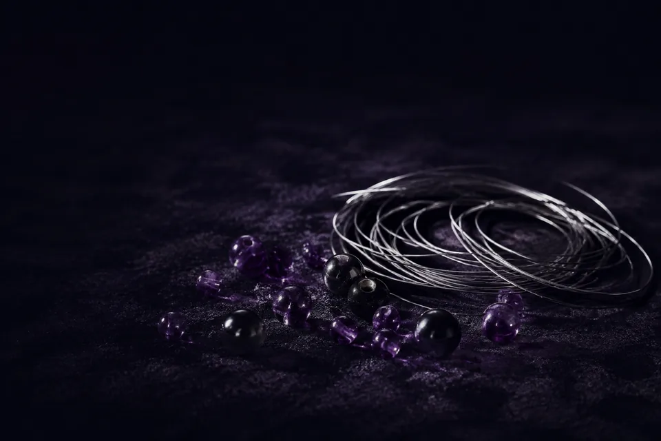 An atmospheric material study of dark violet beads and silver wire on a charcoal surface.